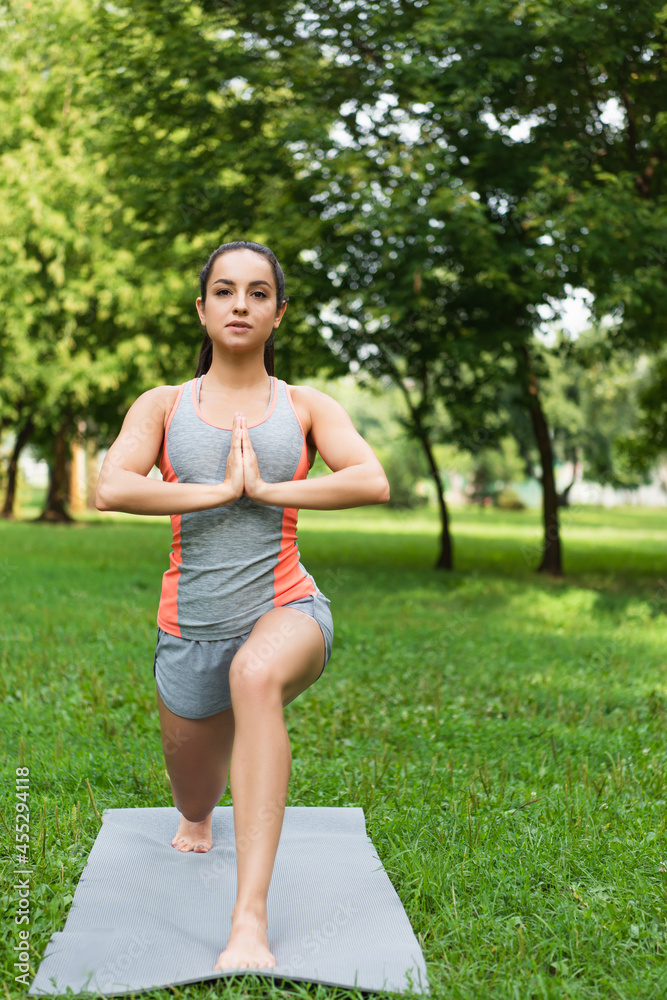 young woman doing low lunge pose on yoga mat in park