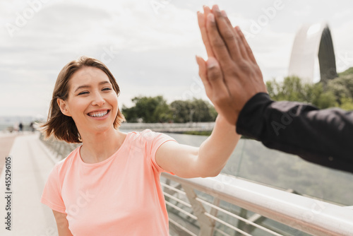 Young woman and man boyfriend and girlfriend friends giving high five after workout training jogging running outdoors on city bridge in the morning. Fitness exercises for slimmimg.