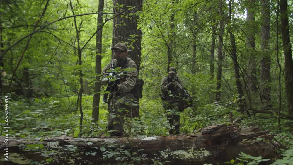Group of soldiers in camouflage moving across dense forest area, machine gunner covering squad while companions getting positions. Sniper shot killing soldier while relocation. Danger military mission Group of soldiers in camouflage moving across dense forest area, machine gunner covering squad while companions getting positions. Sniper shot killing soldier while relocation. Danger military mission