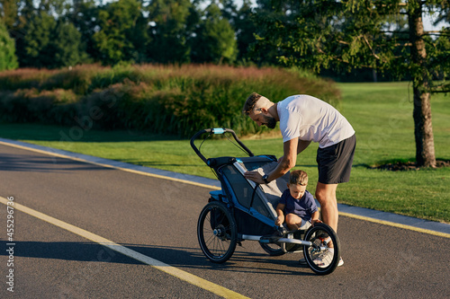Father with his little son with jogging stroller during morning workout and run in city park. Fatherhood, daddy and child. father's day