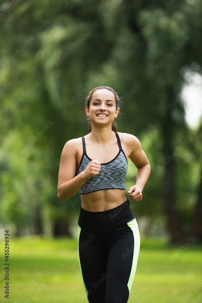 joyful young woman in crop top and leggings jogging in park joyful young woman in crop top and leggings jogging in park
