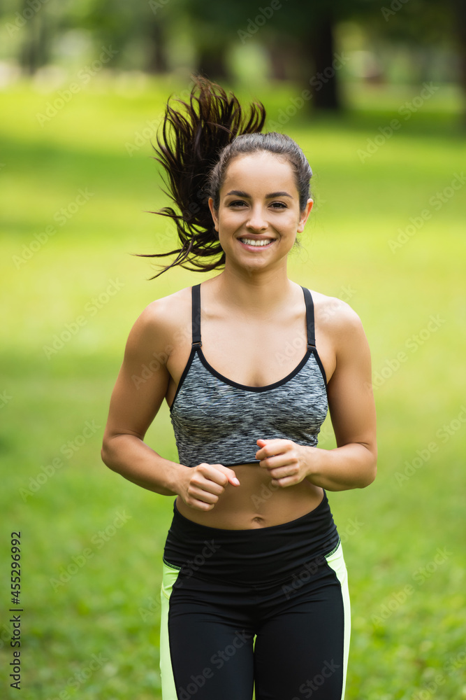 pleased young woman in crop top and leggings jogging in park pleased young woman in crop top and leggings jogging in park