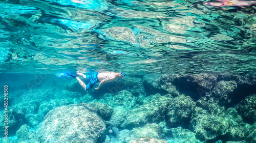 Man snorkeling in the blue sea over a rocky seabed