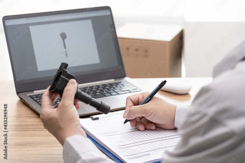 Hand a man write on paper checklist and hold old coil spark plug gasoline engine with laptop computer on table : car service office concept Hand a man write on paper checklist and hold old coil spark plug gasoline engine with laptop computer on table : car service office concept