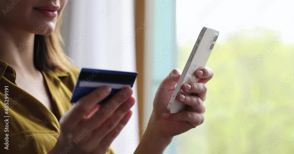 Close up woman standing indoor holds debit card enters digits data makes easy comfort purchase on internet ecommerce web store. Client of electronic services, distance shopping, secure payment concept