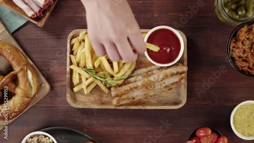 Putting tray with smoked sasuages and fried potatoes top view, pickled cucumbers, bratwursts and fresh pretzels on table. Traditional German Cuisine. Composition of Cooked National Czech Food.  photo