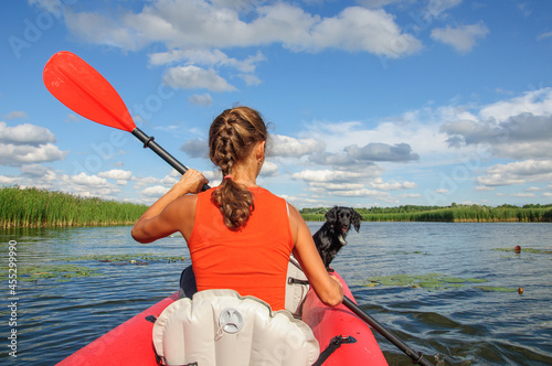 A young sports girl floats on the Zdwyzh River on a red kayak with a black dog Cocker Spaniel. Ukraine