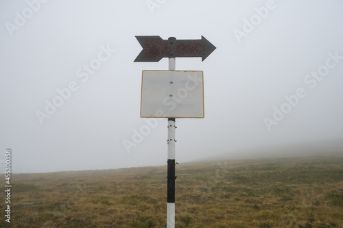 Old and rusty blank hiking sign posts, marking hiking routes up on the mountain on a foggy day.
