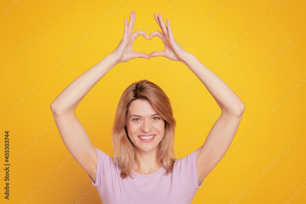 Fototapeta premium Portrait of adorable sweet lady demonstrate heart symbol raise hands on yellow background