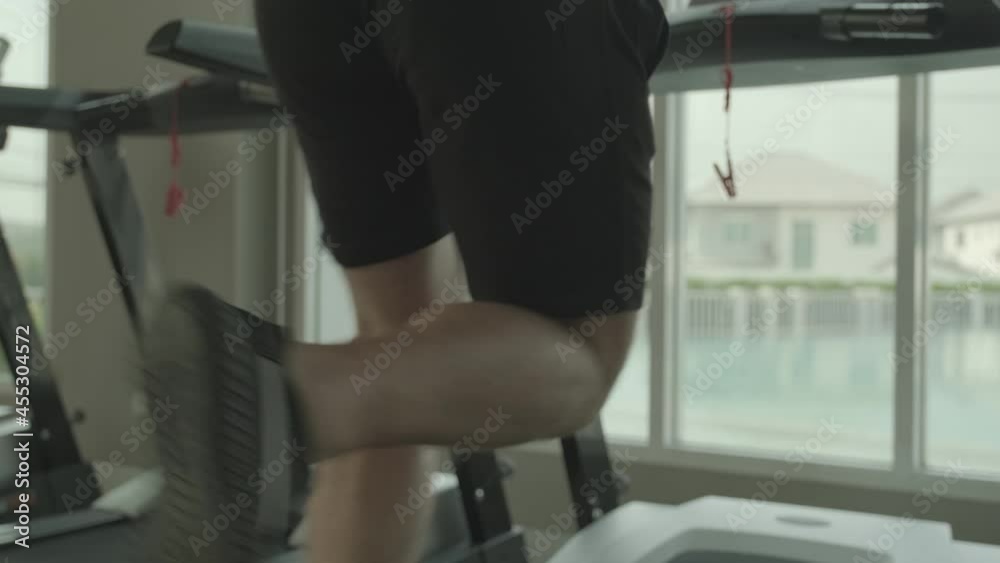 Bottom-to-top back view Slow-motion scene of confident Caucasian athlete wearing headphones and running on the treadmill at a private gym.