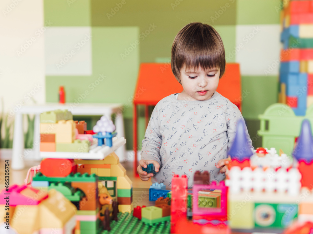 Toddler boy is playing in kidsroom with colorful constructor. Educational toy block in his hands. Kid is busy with toy bricks. Toddler boy is playing in kidsroom with colorful constructor. Educational toy block in his hands. Kid is busy with toy bricks.