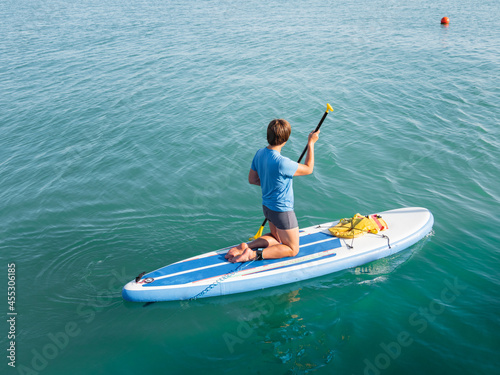 Paddle boarder. Sportsman on knees paddling on stand up paddleboard. SUP surfing. Active lifestyle. Outdoor recreation. Vacation on seaside. © Konstantin Aksenov