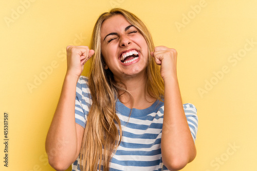 Young caucasian blonde woman isolated on yellow background celebrating a victory, passion and enthusiasm, happy expression.