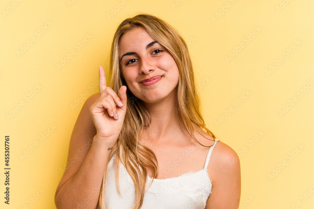 Young caucasian blonde woman isolated on yellow background showing number one with finger. Young caucasian blonde woman isolated on yellow background showing number one with finger.