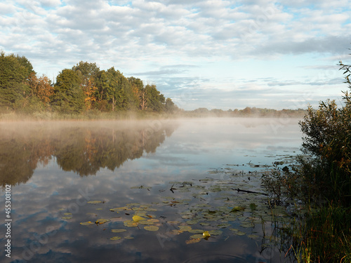 morning fog spreads over the smooth water of the river