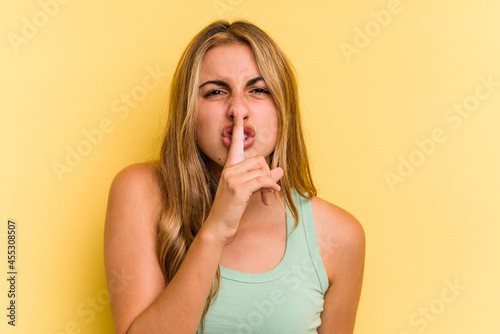 Young caucasian blonde woman isolated on yellow background keeping a secret or asking for silence.