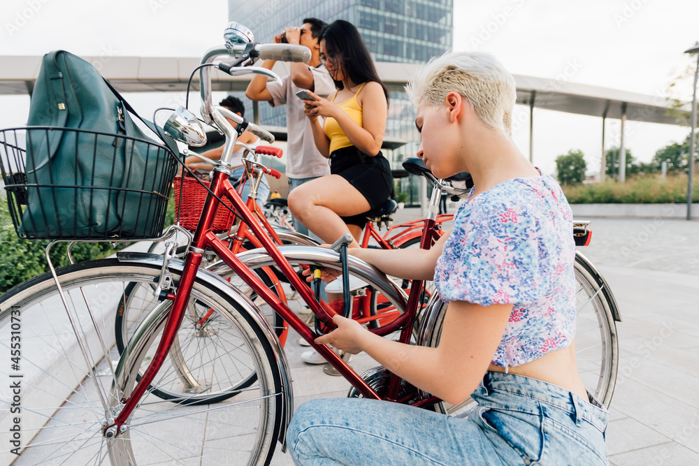 Obraz premium Young caucasian woman fastening bicycle using padlock outdoors