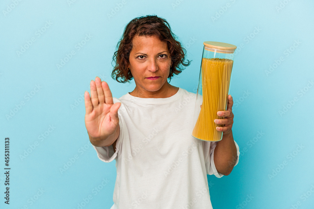 Middle age latin woman holding pasta jar isolated on blue background standing with outstretched hand showing stop sign, preventing you. Middle age latin woman holding pasta jar isolated on blue background standing with outstretched hand showing stop sign, preventing you.