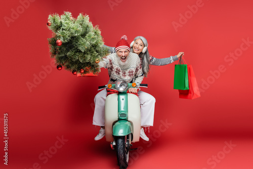 Photography excited middle aged man holding christmas tree near asian wife while riding mope