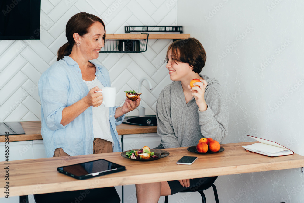 Relationship between a teenager and a parent. Mom and teenage daughter are having breakfast in the kitchen. Relationship between a teenager and a parent. Mom and teenage daughter are having breakfast in the kitchen.
