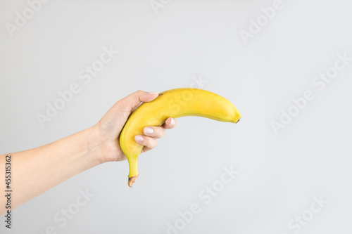 Male hand holding a banana isolated on a grey background. Healthy nutrition diet.