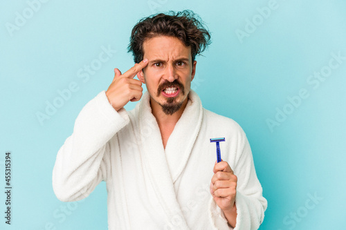 Young caucasian man holding a razor blade isolated on blue background showing a disappointment gesture with forefinger.