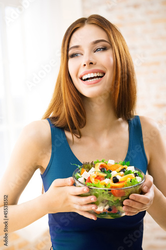 Portrait photo of happy amazed, smiling woman holding greece salad with cheese, indoor. Beautiful girl in casual blue dress - keto dieting, weight loss, healthy eating concept.