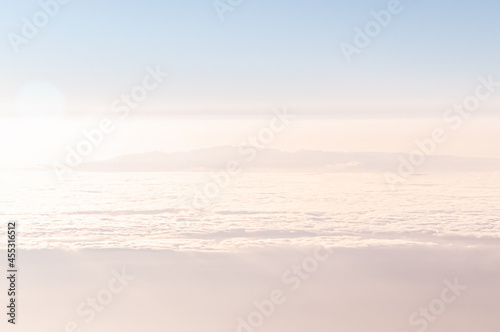Misty Cloudscape. A mysterious island in pink and blue tones surrounded by the ocean and clouds. Fantastic dreamy picture