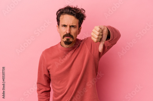 Young caucasian man isolated on pink background showing thumb down and expressing dislike.