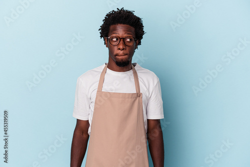Stampa su Tela Young african american store clerk isolated on blue background confused, feels doubtful and unsure