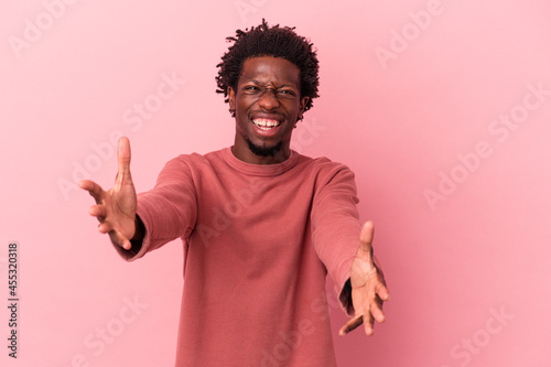 Young african american man isolated on pink background feels confident giving a hug to the camera.