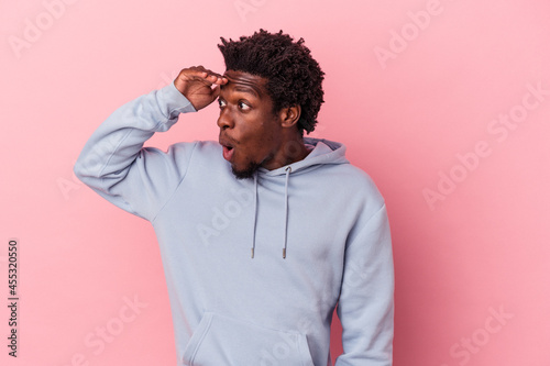 Young african american man isolated on pink background looking far away keeping hand on forehead. © Asier