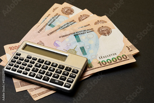 Uzbek money and calculator on black. Pile of Uzbek sums and calculator. Concept of exchange rate. Economic or financial concept photo