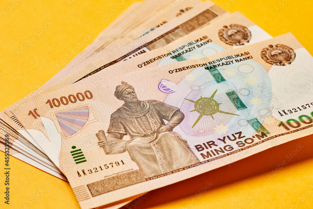 Pile of Uzbek sums on yellow. Uzbek currency money bill. A stack of one hundred thousand Uzbek sum. Uzbek money. 100000 sum