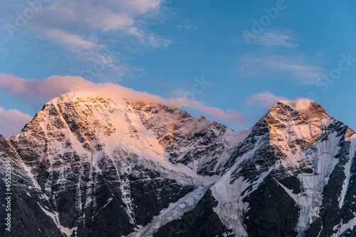 Landscape of high snowy mountains with overhanging glaciers in the sunset rays against a cloudless blue sky