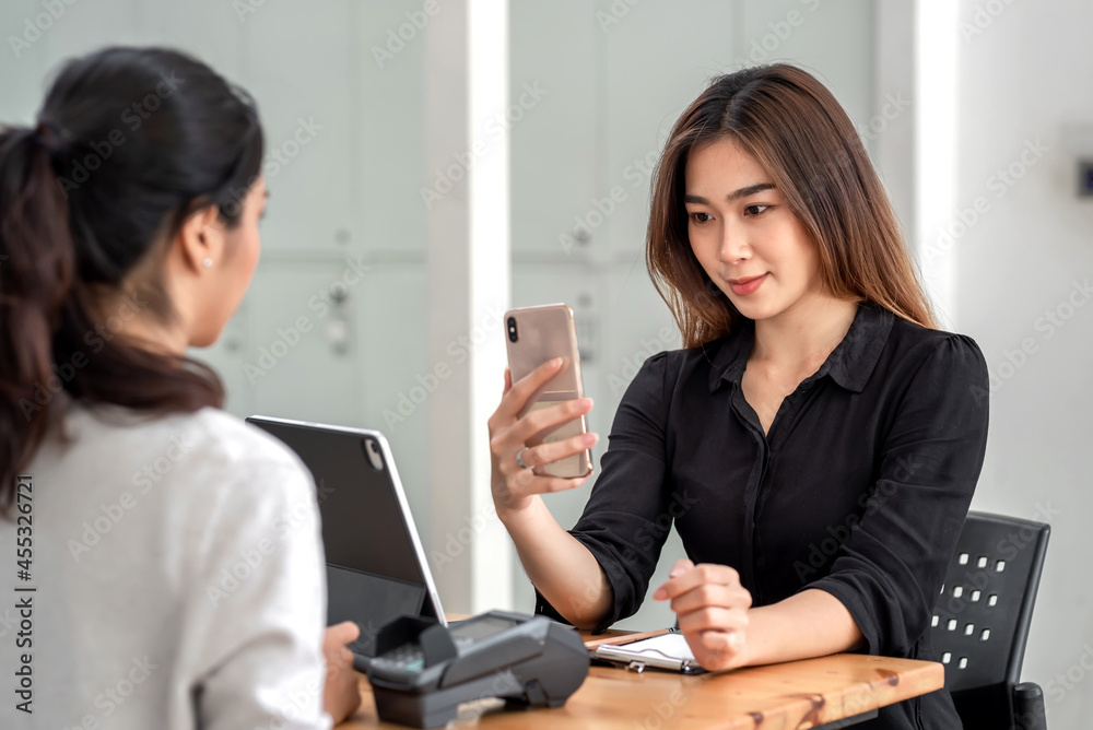 Young Asian businesswoman holding a smartphone to take photos for her colleague with a tablet placed at the office. Young Asian businesswoman holding a smartphone to take photos for her colleague with a tablet placed at the office.
