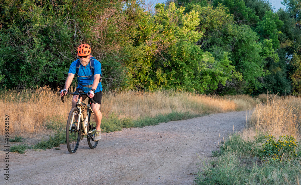 senior male cyclist is riding a touring bike on a gravel trail at Colorado foothills, late summer scenery