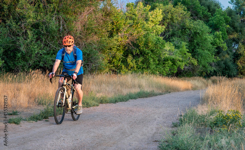 senior male cyclist is riding a touring bike on a gravel trail at Colorado foothills, late summer scenery