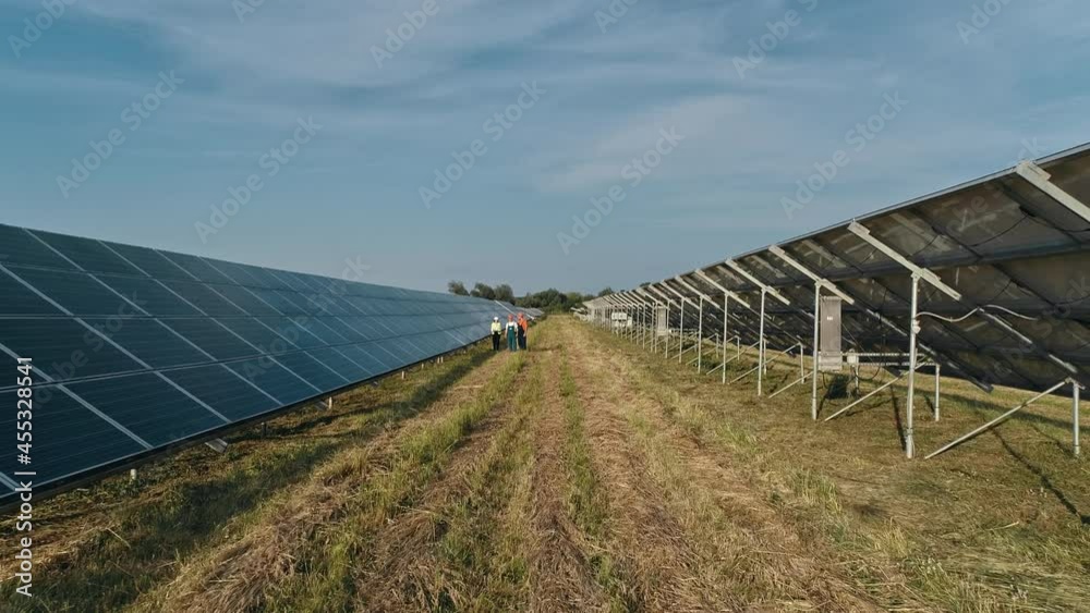 Top view of specialists walking across a solar power plant. Three employees of alternative power plant walking and talking about scheme of solar panels. Teamwork. Group of specialists. Top view of specialists walking across a solar power plant. Three employees of alternative power plant walking and talking about scheme of solar panels. Teamwork. Group of specialists.