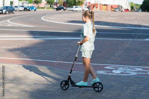 Beautiful teen girl rides around town on a scooter sunny summer evening. © queen1987