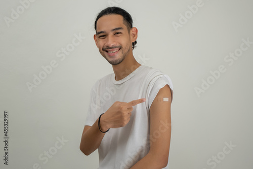 Happy Asian man showing his arm and bandage after they get a vaccine.