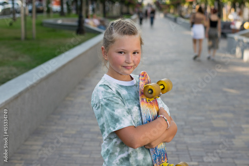 Beautiful girl with a skateboard in the park on a warm summer evening.