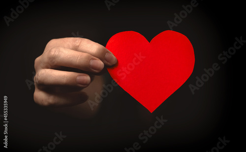 Hand holding red heart on black background. Love from the dark concept. Health insurance, organ donor day, charity photo