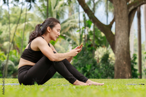 Young woman searching for yoga poses on the internet via mobile phone on mat in outdoor park. © skarie
