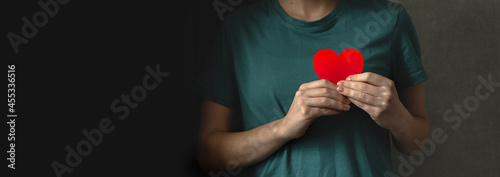 Red heart in hands. Banner with black background. Young lady giving her love concept photo