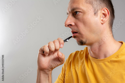 Side view of Handsome bearded man with healthy teeth isolated on a grey background. Dental hygiene - man holding toothbrush with toothpaste in hand. Morning routine of washing the teeth.