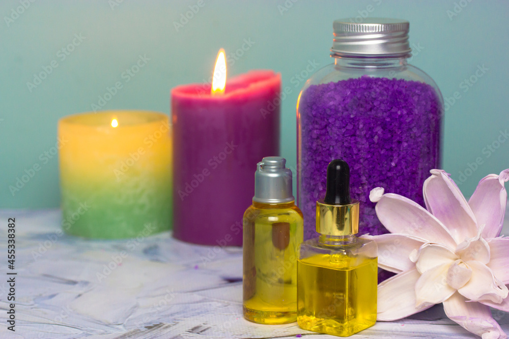 Bottles with essential oil for hair, face and body care, violet lavender sea salt for bath in a bottle, burning candles in the background and pink lotus flower. Spa treatments. Cosmetic products. Bottles with essential oil for hair, face and body care, violet lavender sea salt for bath in a bottle, burning candles in the background and pink lotus flower. Spa treatments. Cosmetic products.