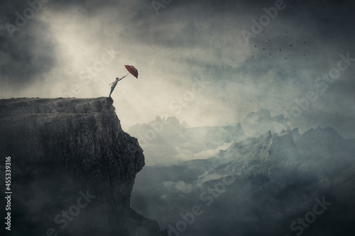 Fearless person on the edge of a cliff determined to catch his umbrella and fly away over abyss. Surreal adventure, conceptual scene for achievement and purposefulness photo