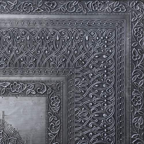  Decorative asian chasing art framework with arabesque pattern in form of embossing on metal.Textured metal frame backdrop with ancient oriental floral wavy ornament. Carved silver black background.