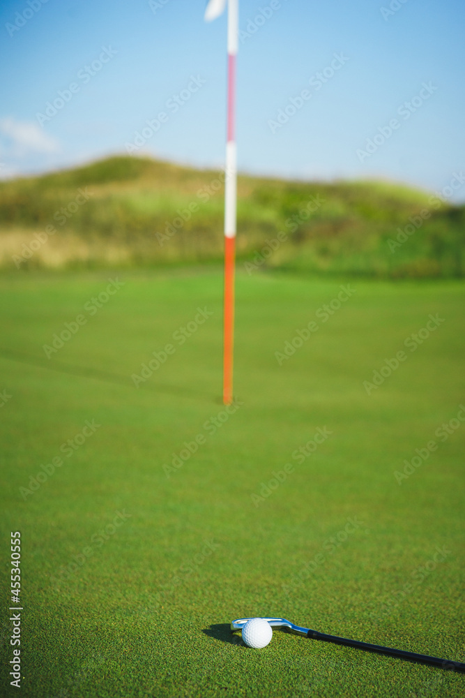 Obraz premium Golf ball and putter on the green grass next to the hole.